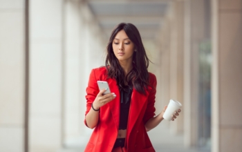 Young,Asian,Woman,With,Smartphone,Standing,Against,Street,Blurred,Building