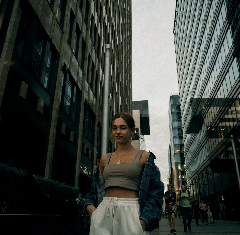 Woman in Crop Top with Denim Jacket Walking on the Street Between High Rise Buildings