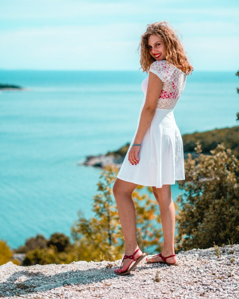 woman in white dress standing on rocky shore during daytime