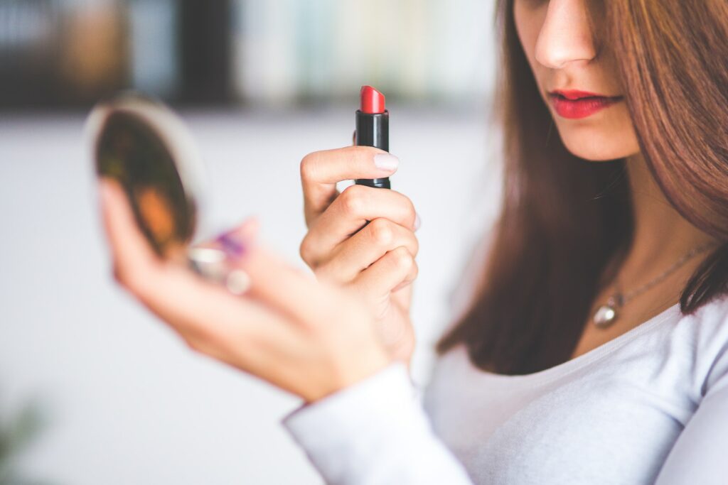 Woman with brown hair doing lipstick and holding little mirror