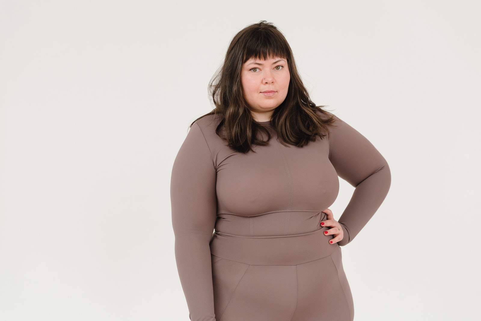 Plus size female in activewear keeping hand on waist and looking at camera against white background