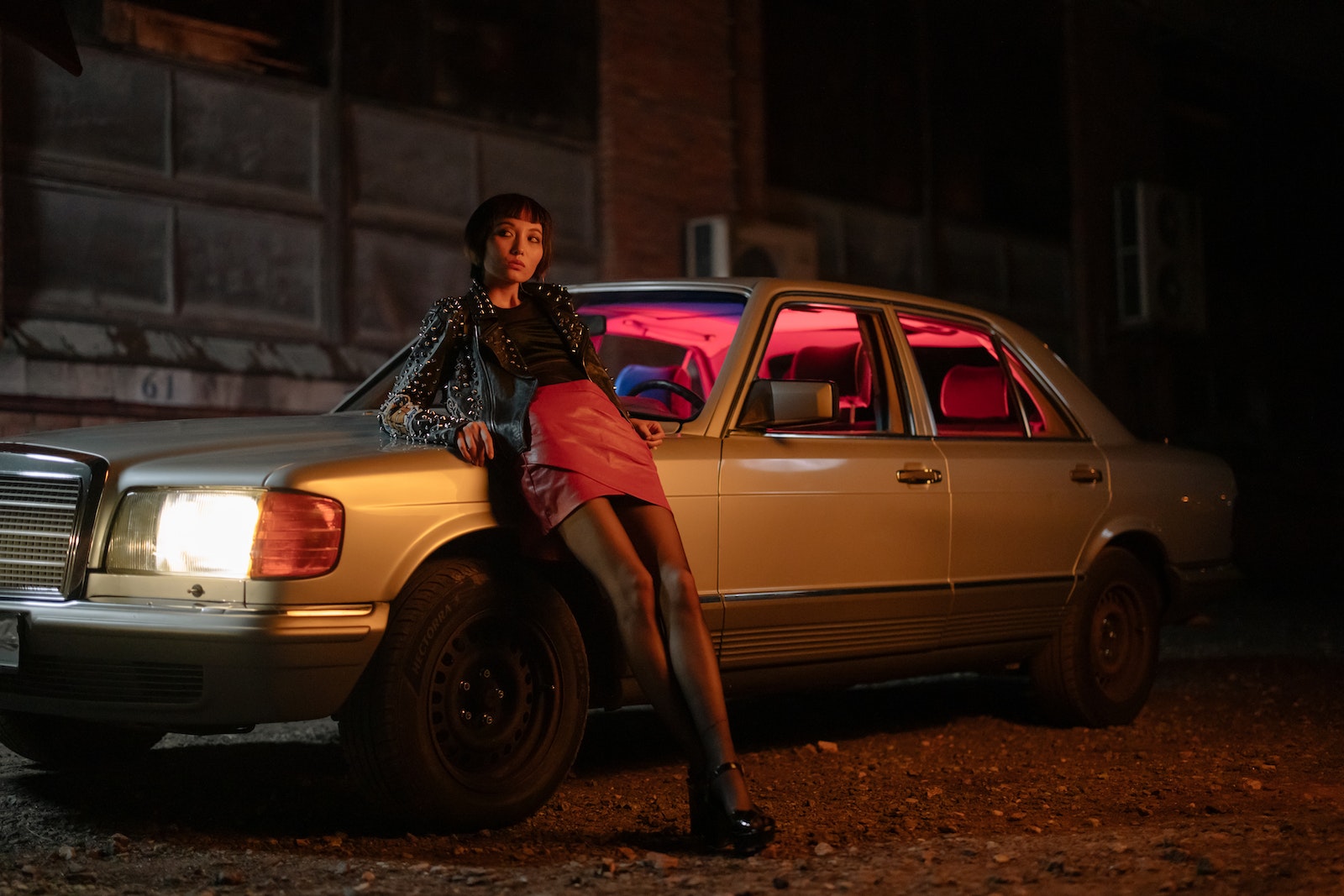 Woman in Black Leather Jacket and Pink Skirt Sitting on Brown Sedan