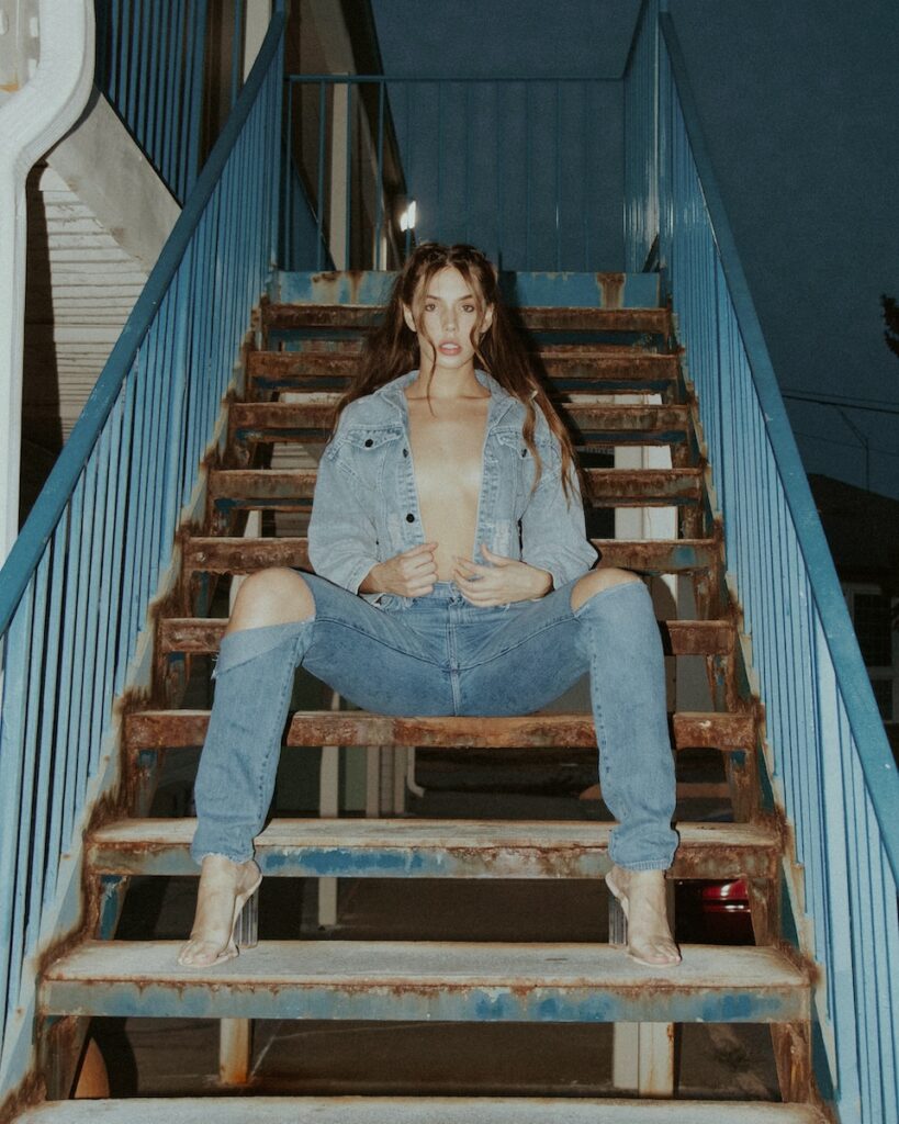 woman in white shirt and blue denim jeans sitting on brown wooden staircase