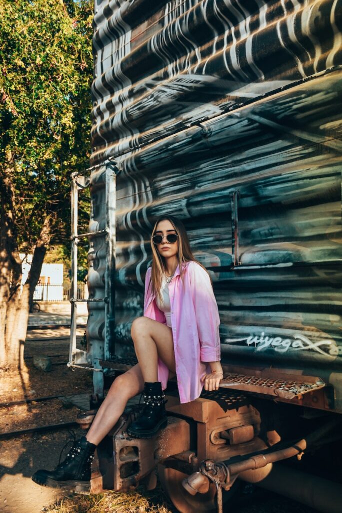 Young Woman in Sunglasses Sitting Outside of a Rusty Trailer