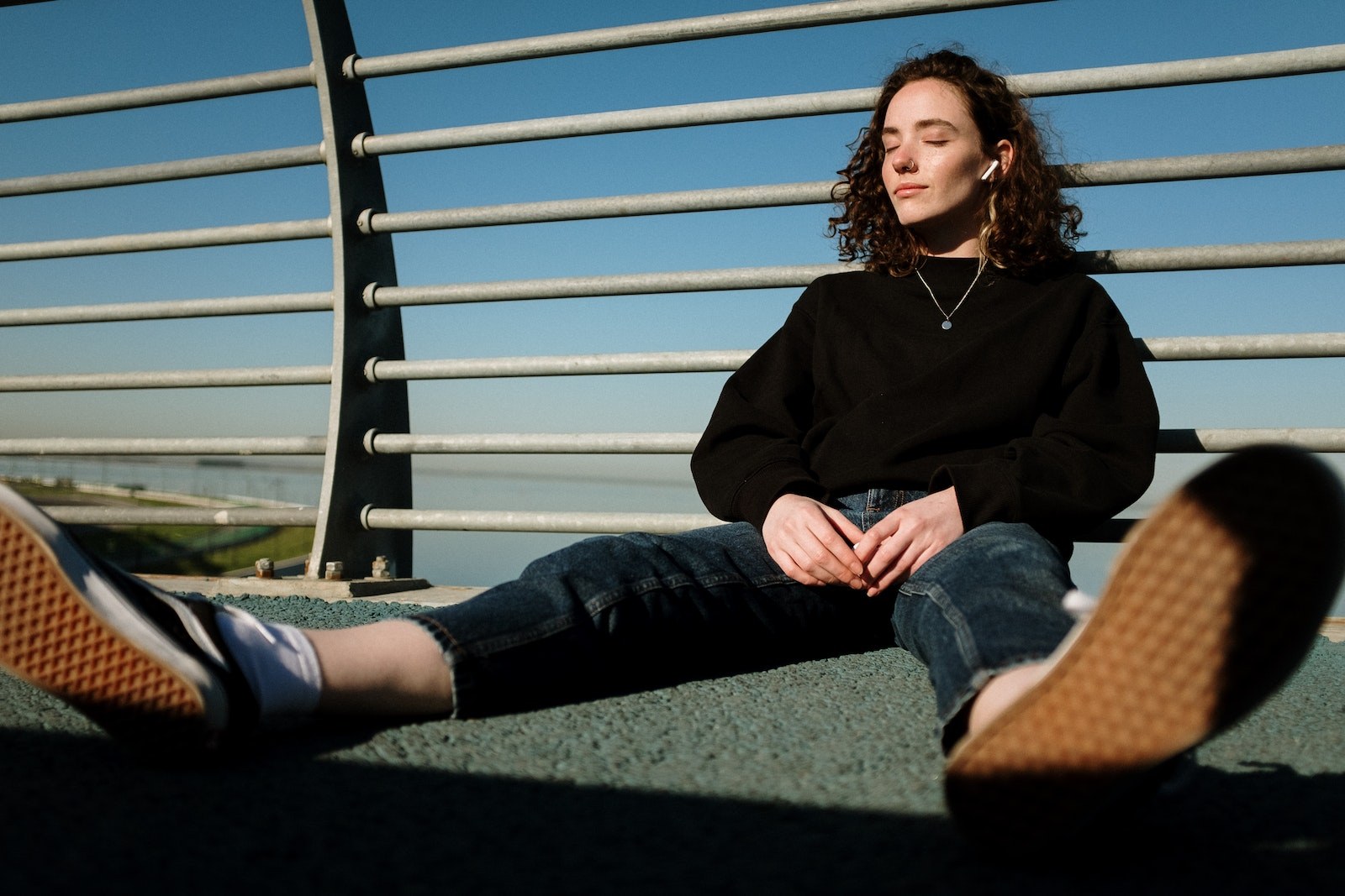 Woman in Black Long Sleeve Shirt and Blue Denim Jeans Sitting on Green Grass Field during