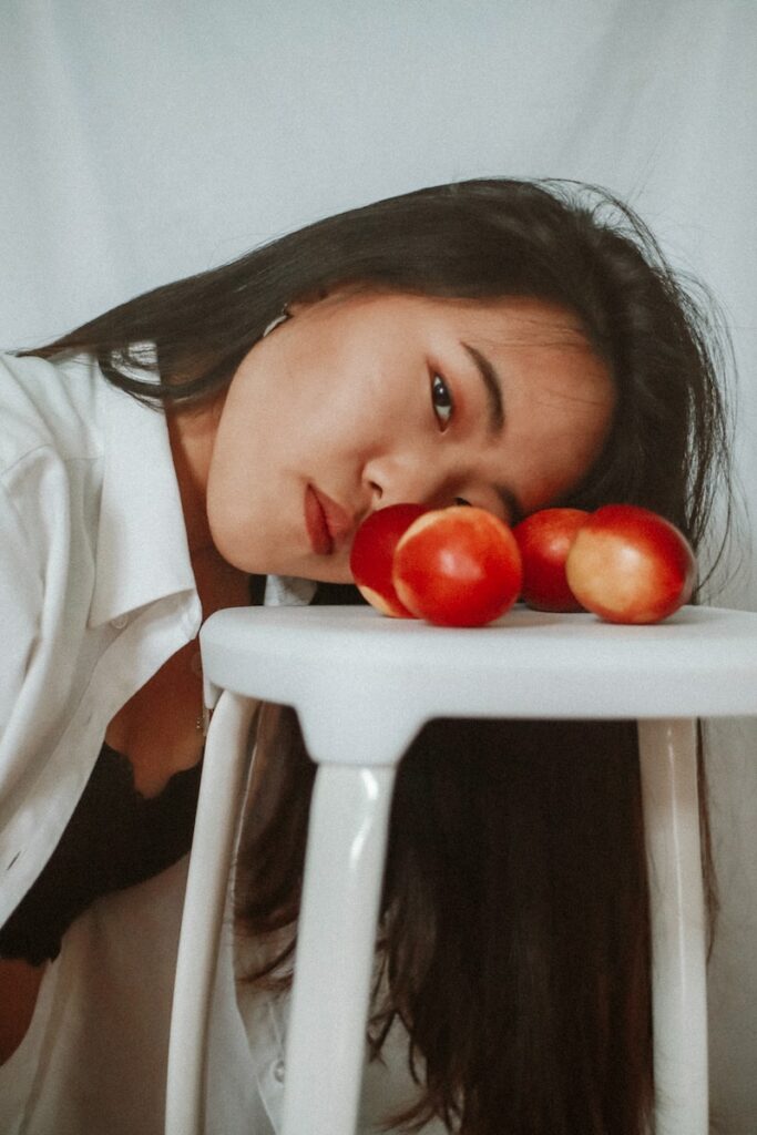 girl in white shirt sitting on white chair with red tomato on her head