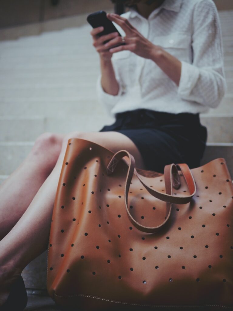 woman sitting on concrete stair beside brown leather tote bag
