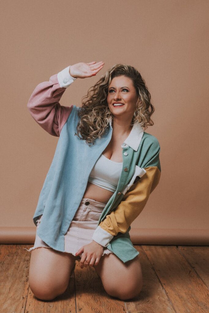 Smiling Model in a Colorful Corduroy Shirt and Frayed Mini Skirt Kneeling on the Floor