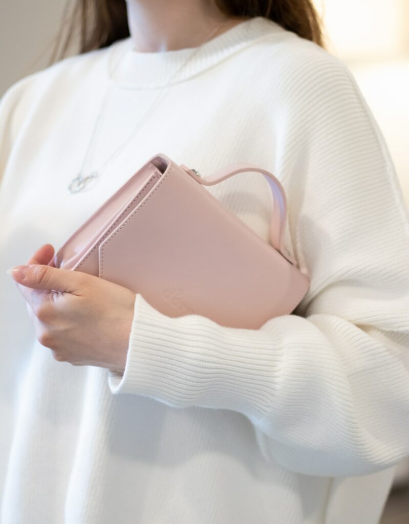 a woman in a white sweater holding a pink purse