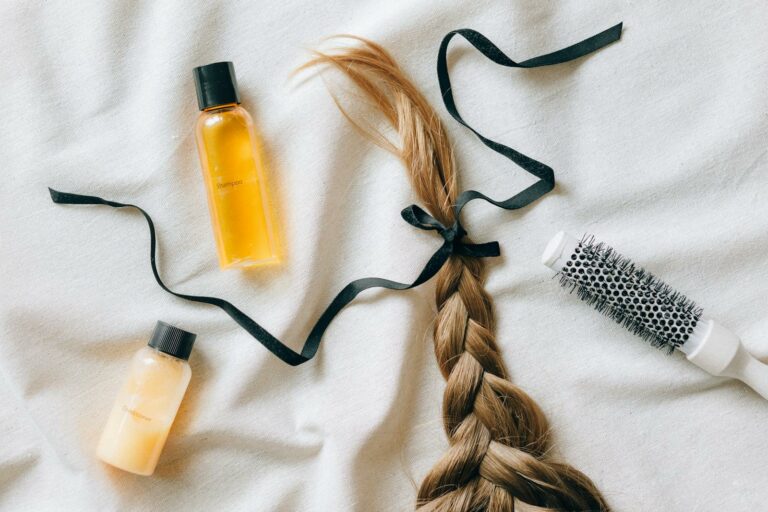 A Braided Hair with Ribbon on White Textile Beside a Brush and Bottles