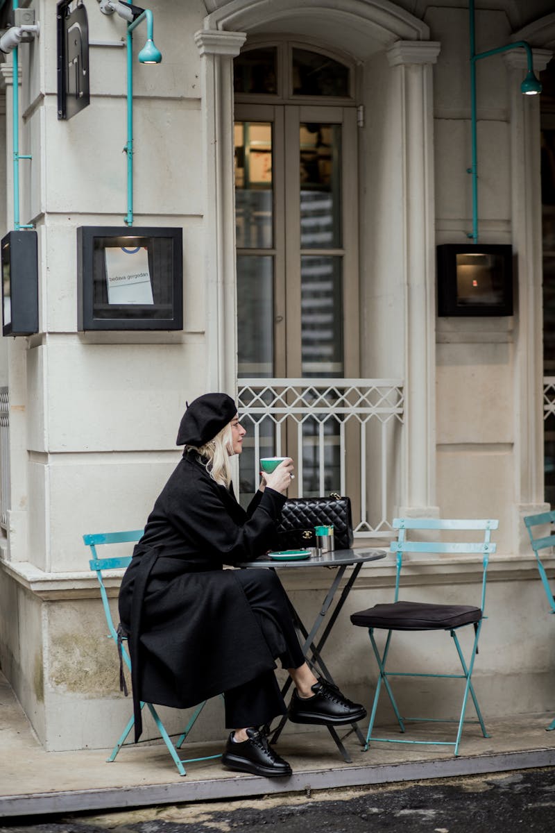 Woman in Black Coat Sitting at Cafe on Street in Town