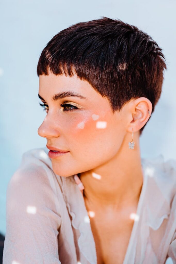 Content female with short hair looking into distance while siting on gray background with bright sparkles on face