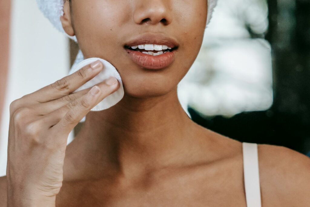 Crop anonymous ethnic female with pure skin touching cheek with cotton disk during daily routine at home